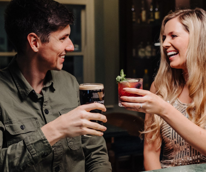 Happy couple enjoying each other's company at a bar, holding a cocktail and a pint of Guinness.