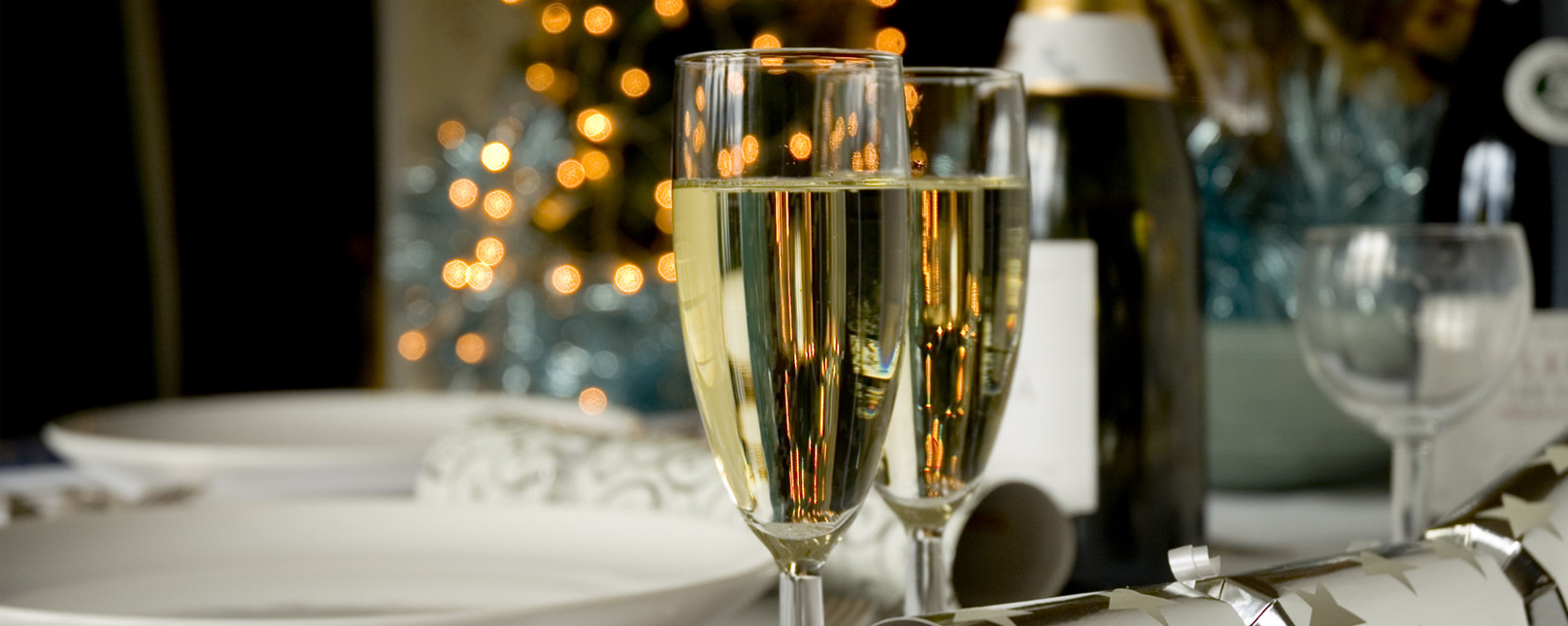 Enjoy the award winning Hillyard experience this Festive season Two champagne glasses sitting one a white table with a champagne bottle and some plates and cutlery within the backdrop